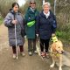 three smiling ladies standing together one witha white cane and one with a guide dog.