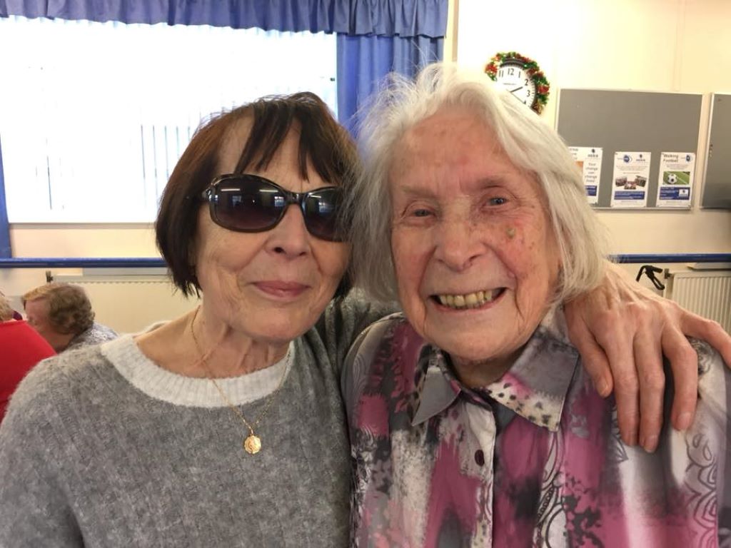 Two smiling ladies with thei arms around eaach others shoulders.