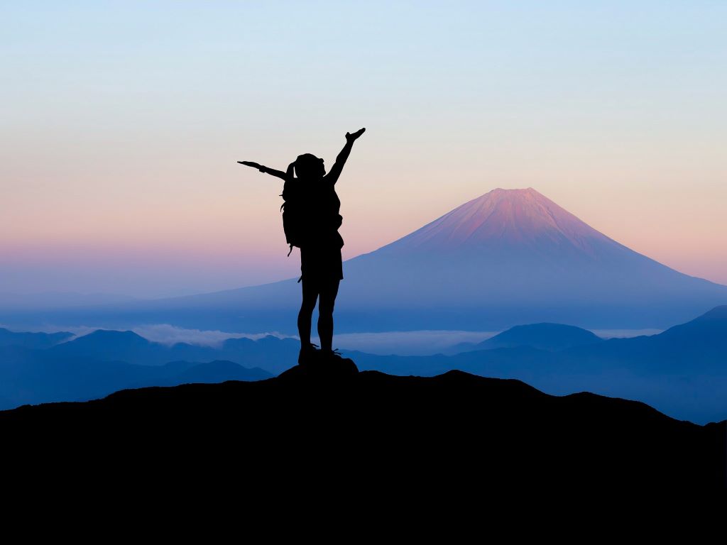 A silhouetted standing on top of a mountain with their arms in the air.