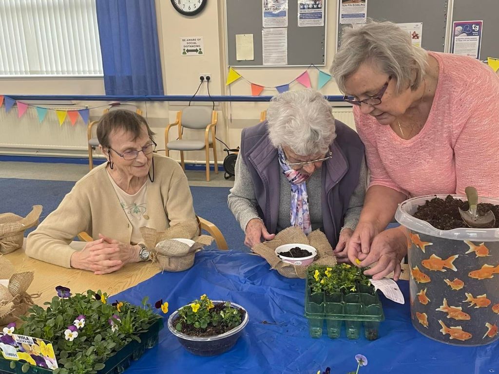 Three ladies potting small seedling plants in pots.