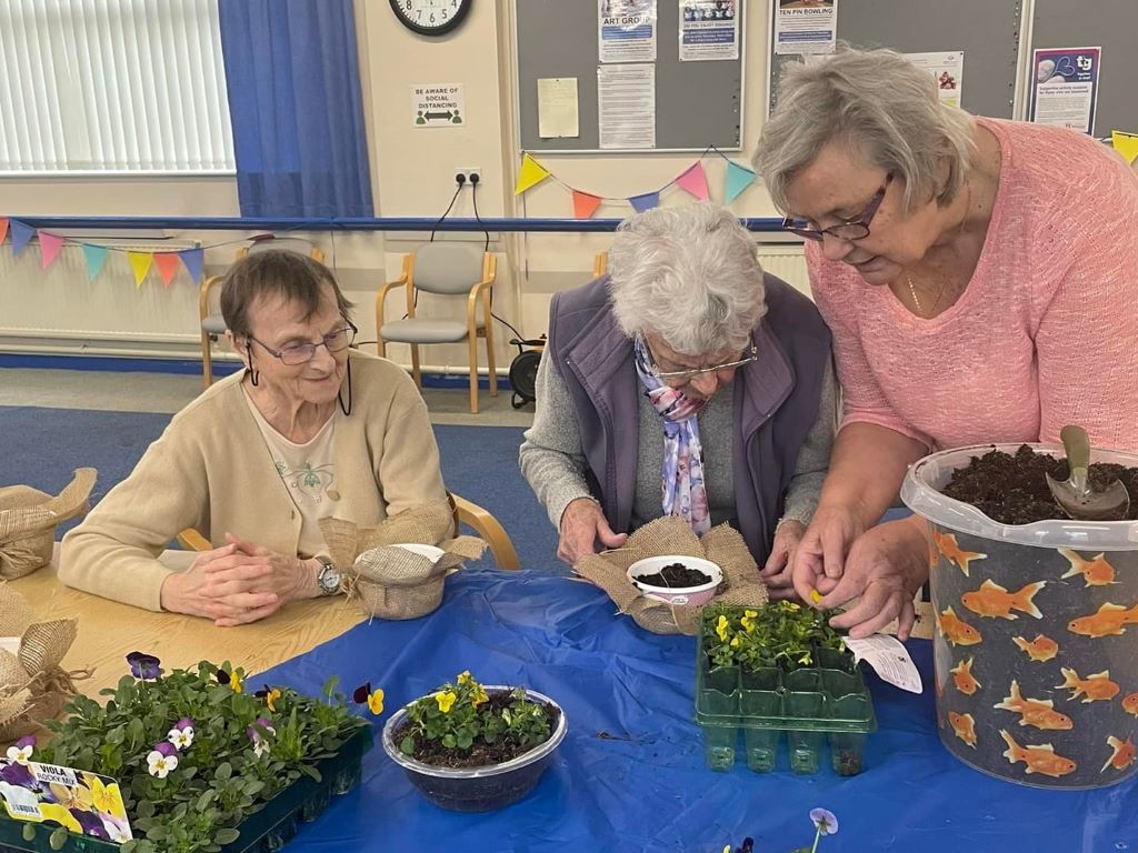 Three ladies potting small seedling plants in pots.