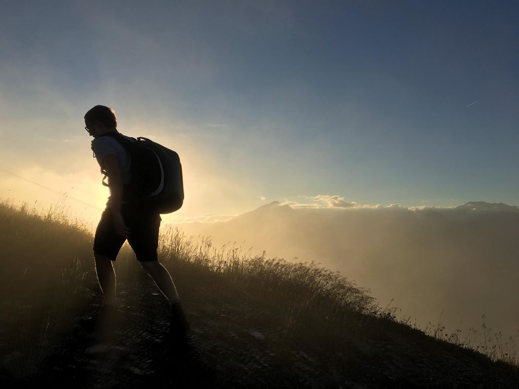 A man walking up a hilldside silhouetted by the settingsun.