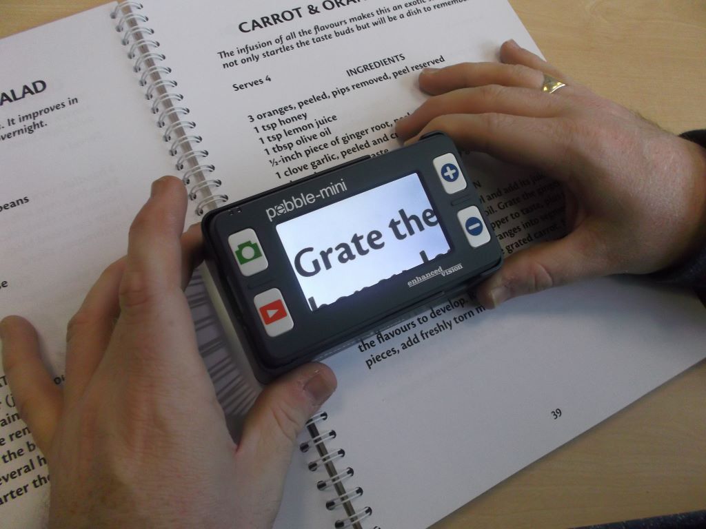 Two hands holding a digital magnifier against a page of writing.