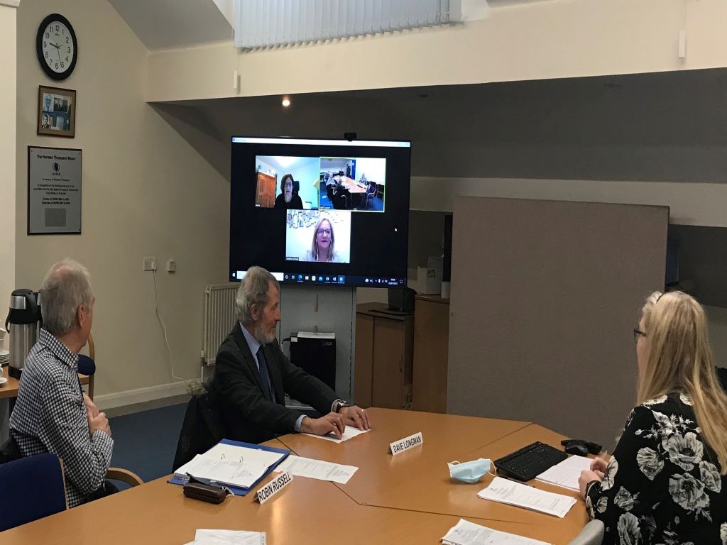A group of people sitting arouns a table watching a television screen