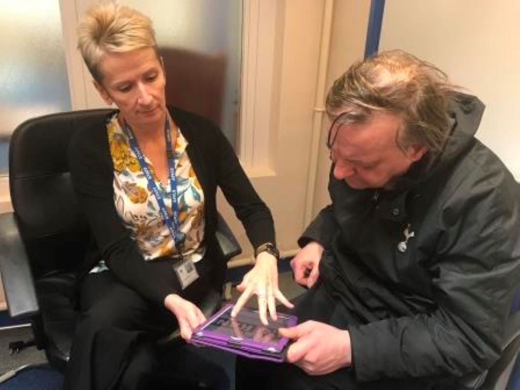 a lady demonstrating a piece of technology to a gentleman both sitting down.