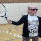A young girl wearing dark glasses holding a tennis racket