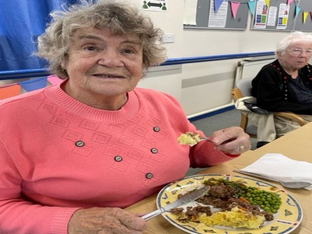 A smiling lady sitting eating a meal.