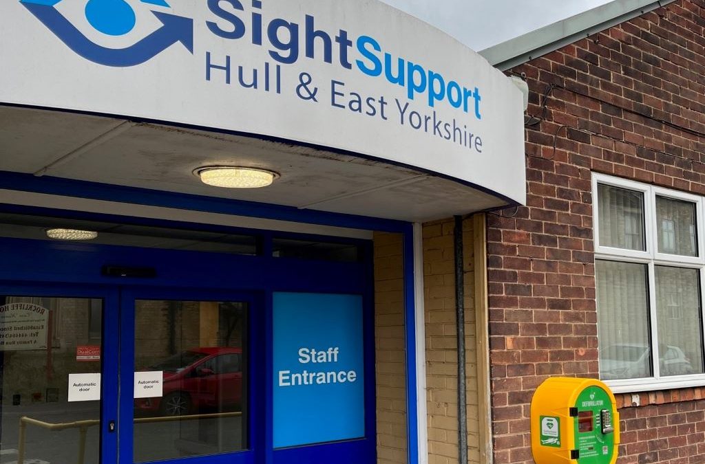 An entrance door with a sign above which reads Sight Support Hull and East Yorkshire and a large yellow box on the wall next to it.