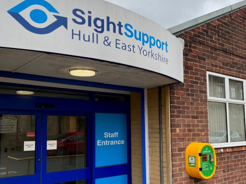 An entrance door with a sign above which reads Sight Support Hull and East Yorkshire and a large yellow box on the wall next to it.