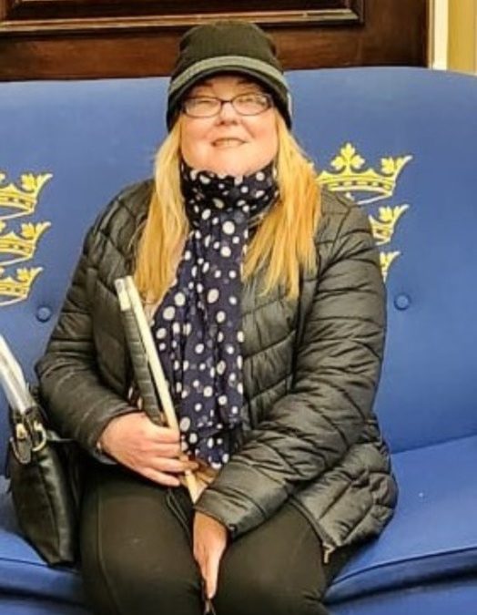 A smiling lady holding a white cane.