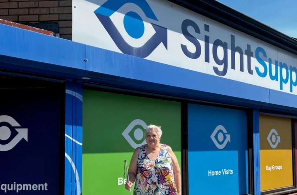 A lady walking in from of Sight Support's building using a white cane.