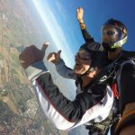 A close up photo of two people skydiving in tandem giving a thumbs up signal.