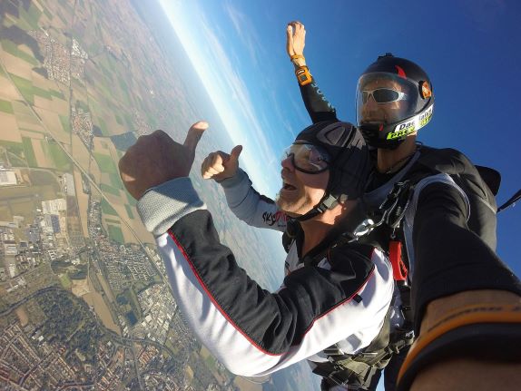 A close up photo of two people skydiving in tandem giving a thumbs up signal.