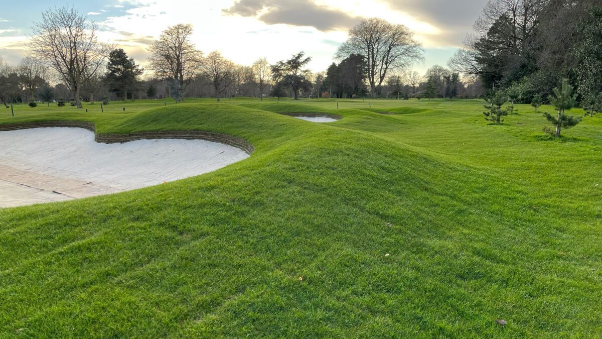 Image of a golf course featuring a green and a sand bunker in the foreground.