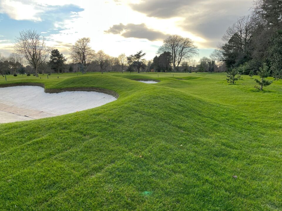 Image of a golf course featuring a green and a sand bunker in the foreground.