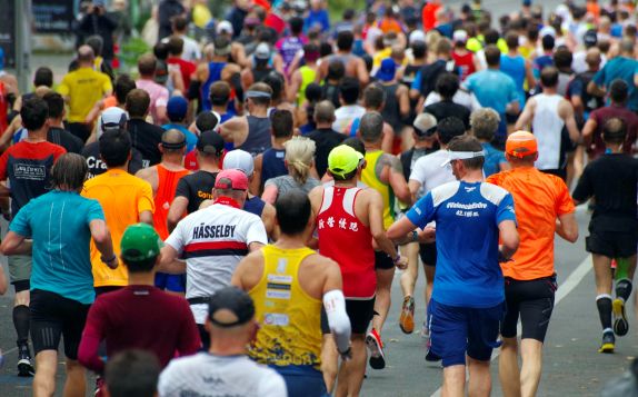 A group of runners in different coloured running vests viewed from behind.